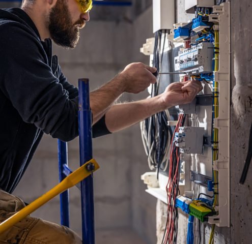 male-electrician-works-switchboard-with-electrical-connecting-cable